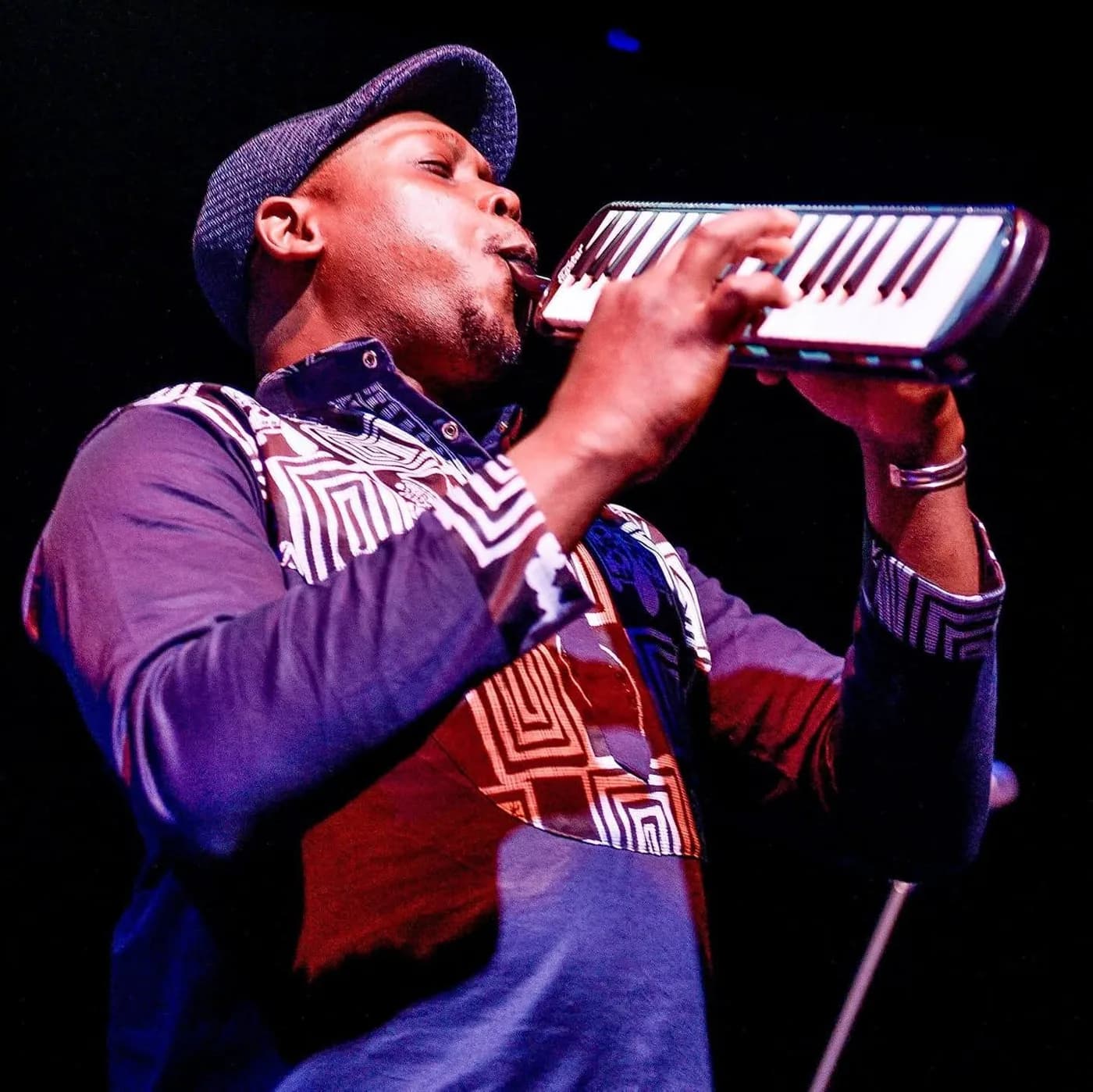 Serge Tebu playing melodica on stage under blue and violet lighting