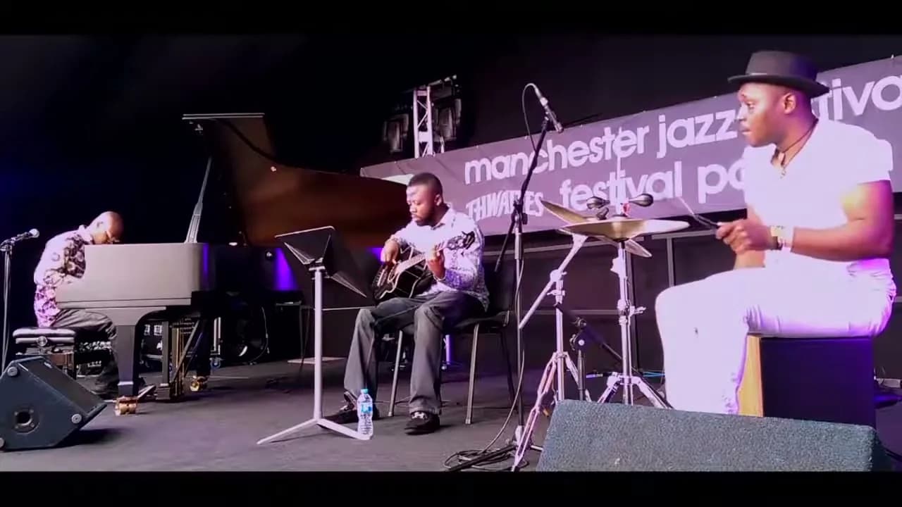 Piano, guitar and cajón on an outdoor stage under a Manchester Jazz Festival banner