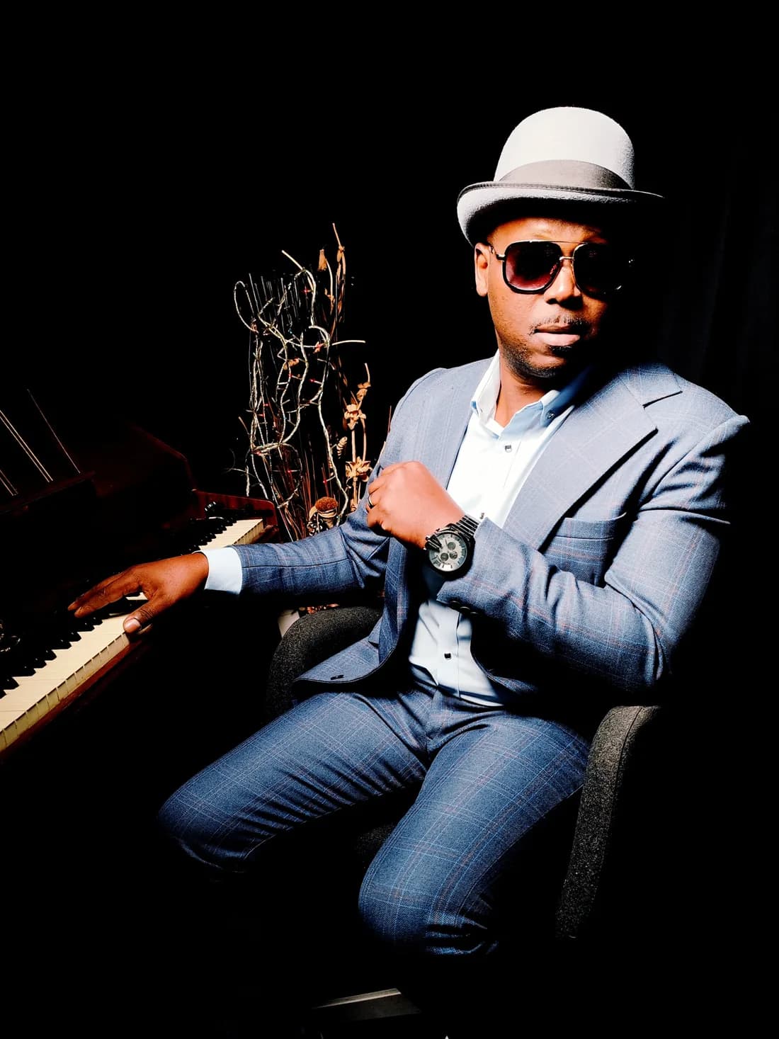 Serge Tebu seated at the piano in a hat and sunglasses, one hand on the keys