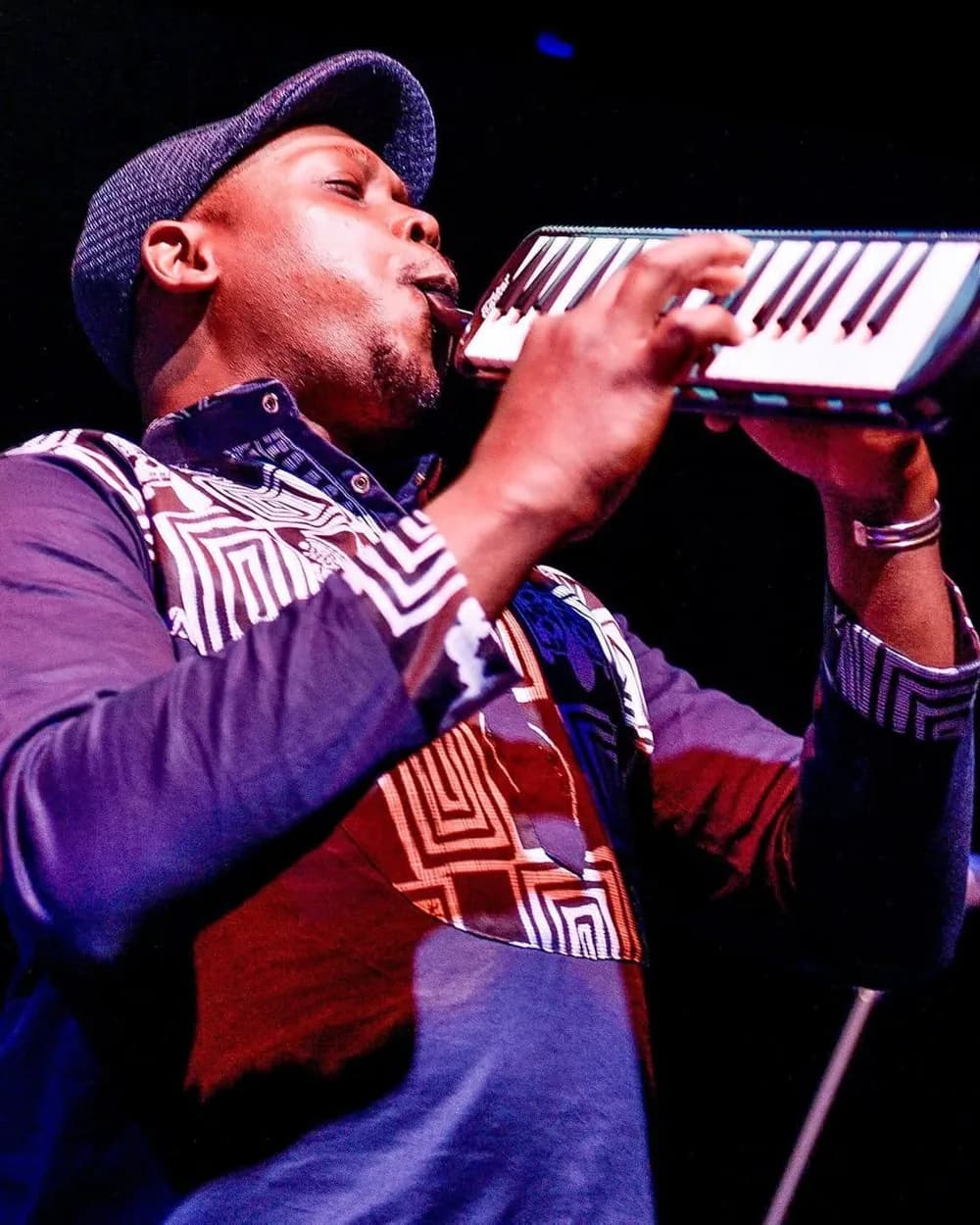 Serge Tebu playing melodica on stage under blue and violet lighting