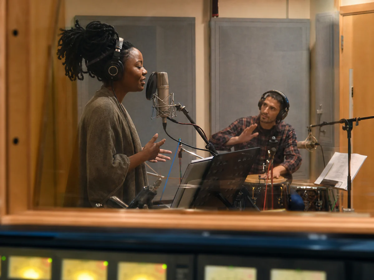 Vocalist and percussionist recording together through studio glass